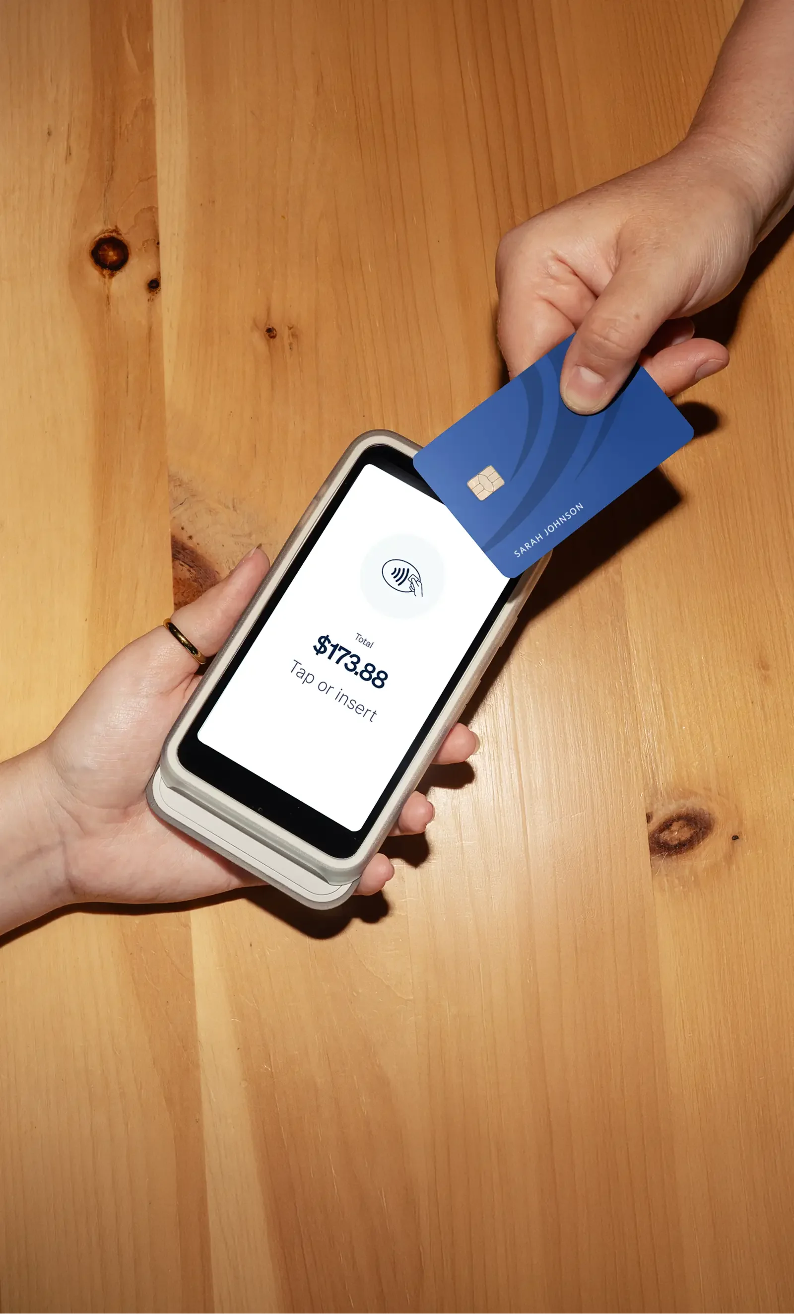 Hand holding a payment card above a Tee On payment terminal on a counter.